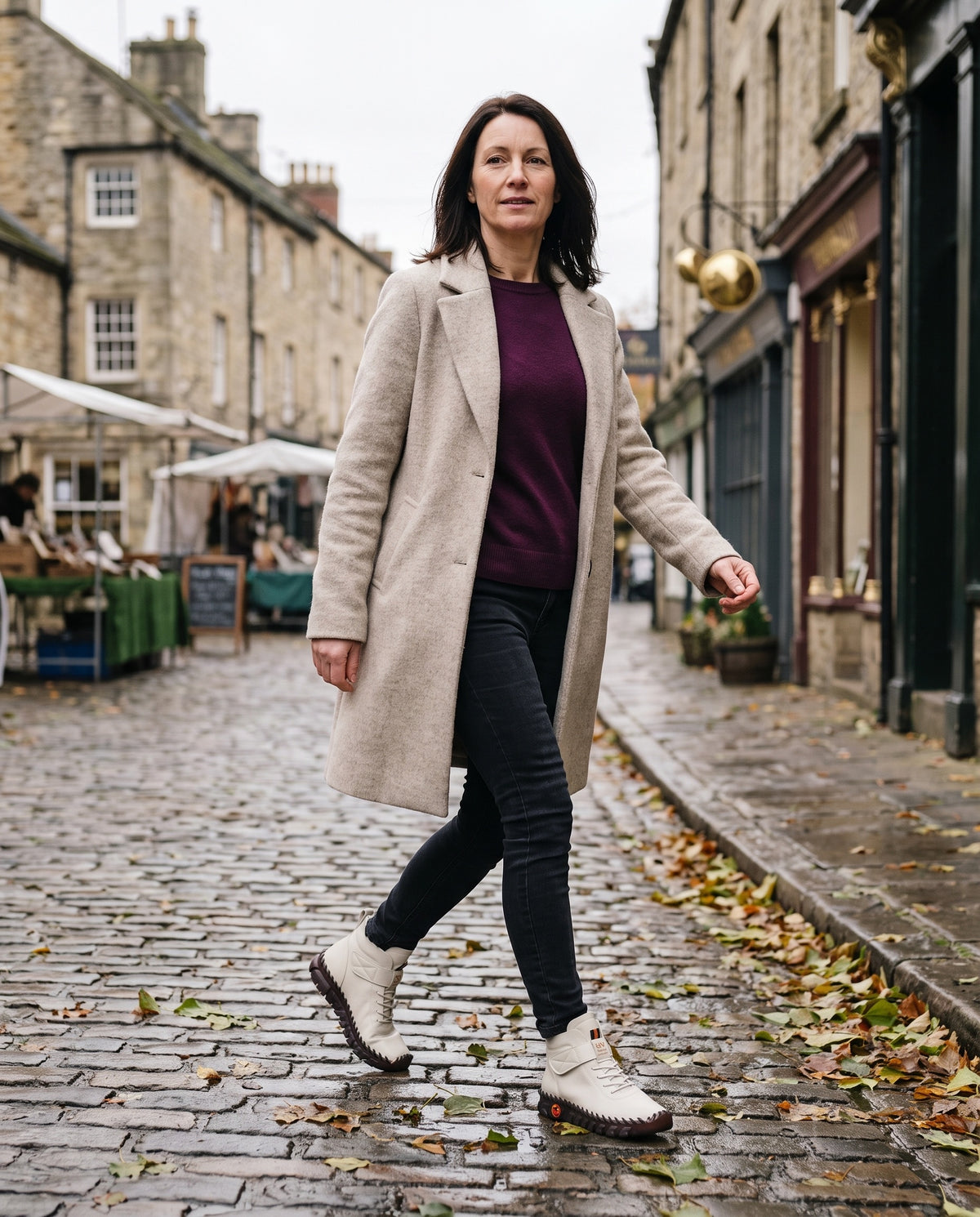 Woman in a long coat walking down a cobbled English street
