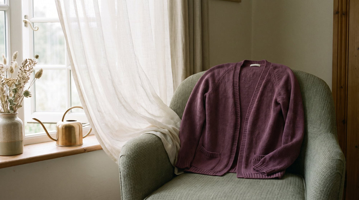 A light open cardigan hanging over a chair beside an open window with a breeze lifting a sheer curtain Image