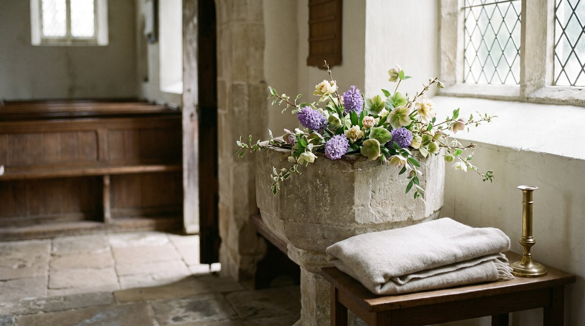 The interior of a quiet village church with a stone font and spring flowers, soft window light Image