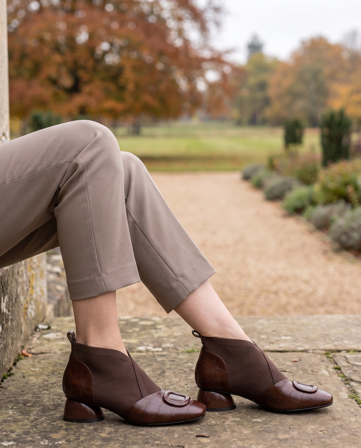 Close-up of feet wearing the orthopaedic knit ankle boots with low block heel, seated on a stone step