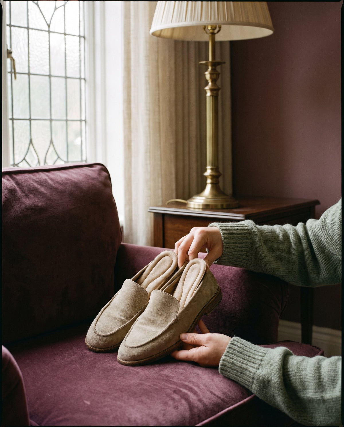 Hands holding a pair of soft beige loafers on a plum armchair Image