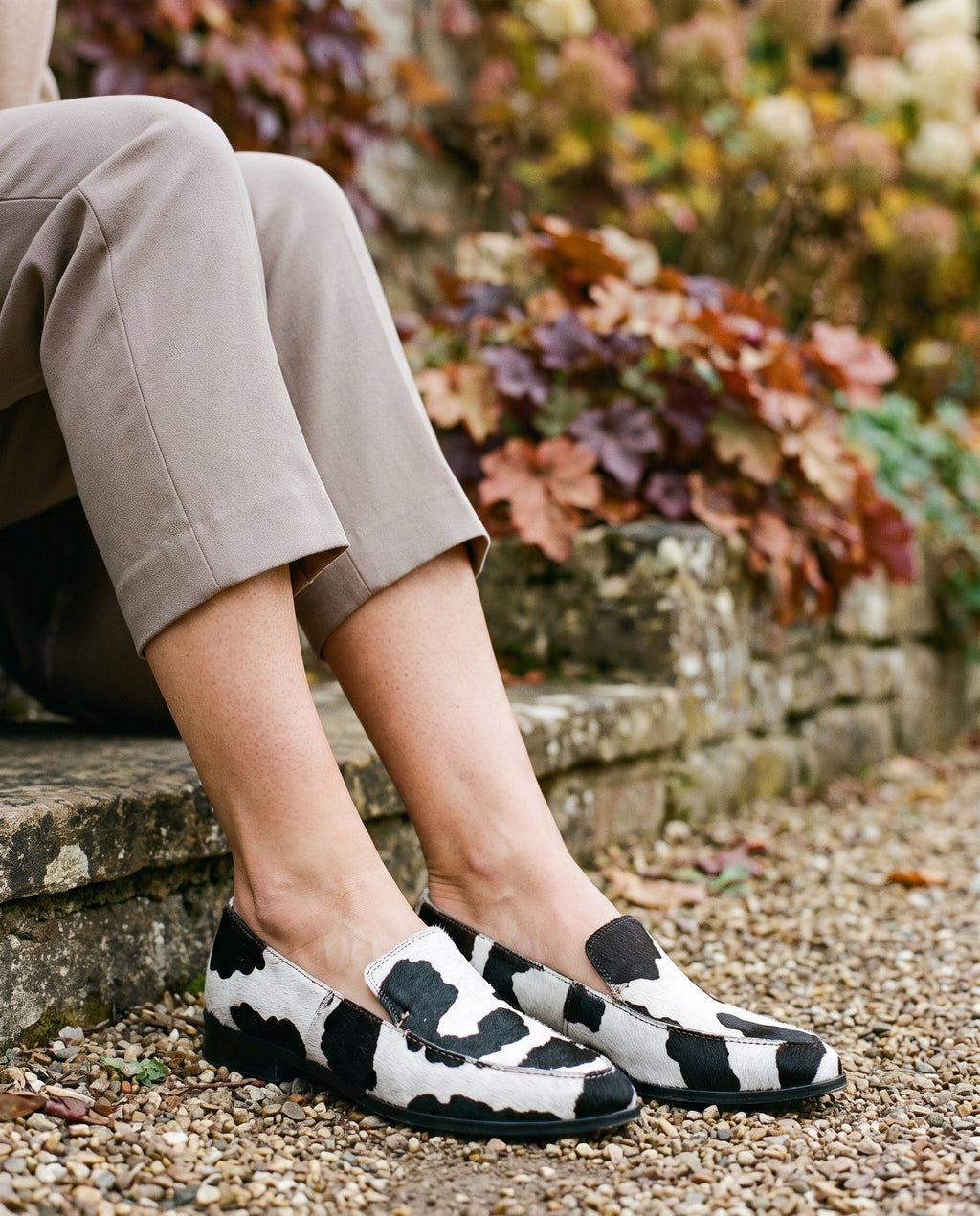 Close-up of feet wearing the pointed cow print loafers, flat sole, seated on a stone step