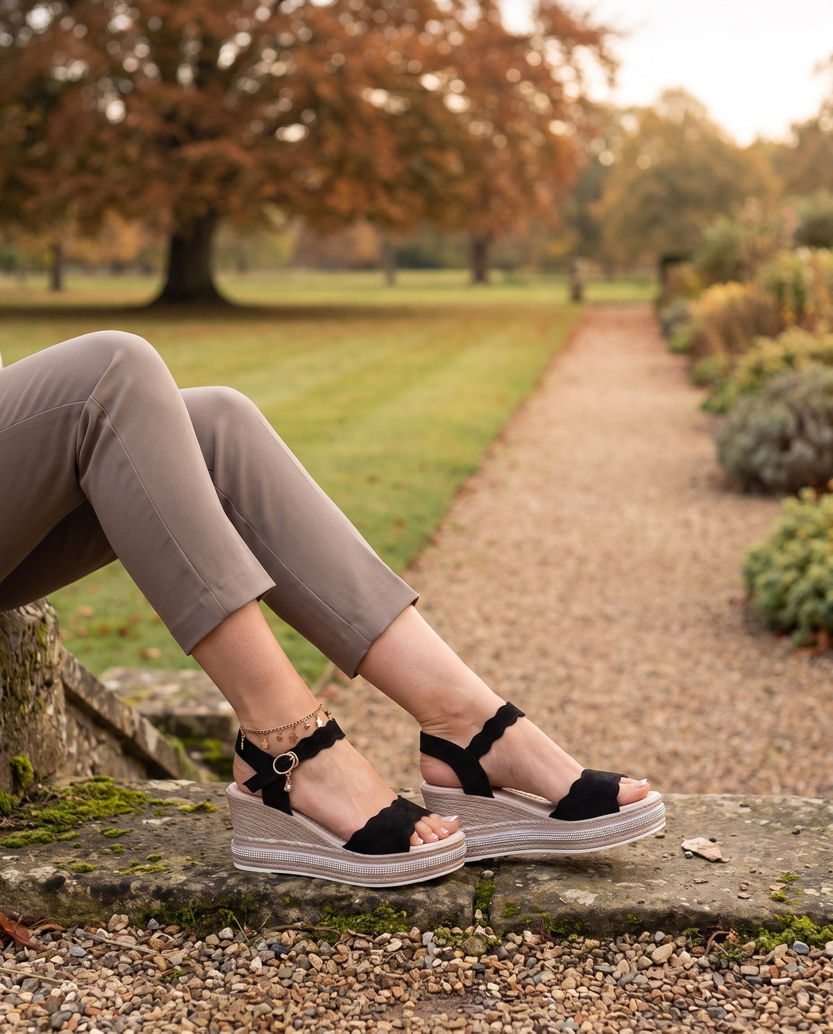 Close-up of feet wearing the orthopaedic wedge sandals, scalloped ankle strap, seated on a stone step Image