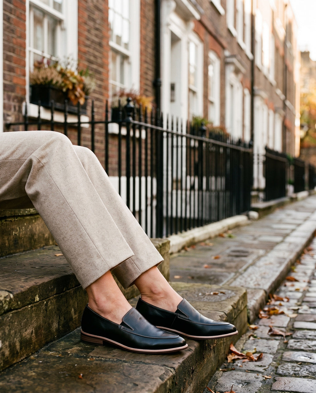 Close-up of feet wearing the orthopaedic pointed slip-on loafers, glossy finish, seated on a stone step