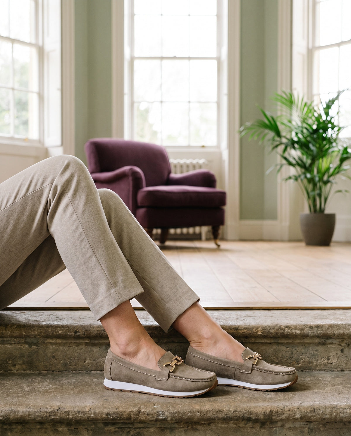 Close-up of feet wearing the suede-look loafers with gold-tone metal trim, seated on a stone step