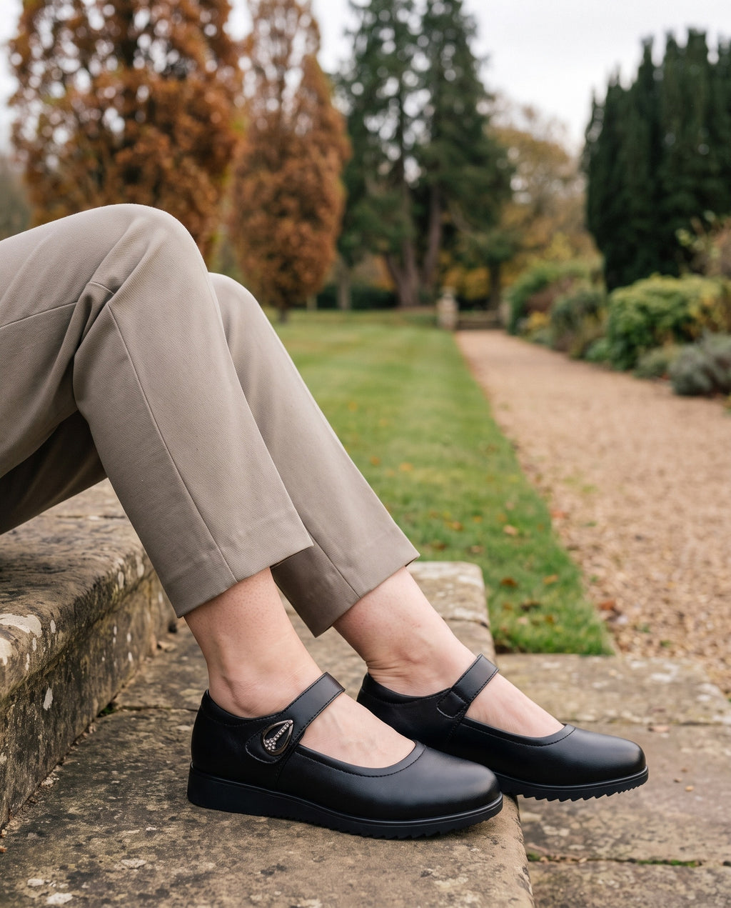 Close-up of feet wearing the orthopaedic mary jane flats with adjustable strap, seated on a stone step