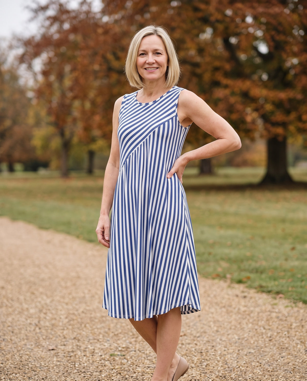 Woman wearing the sleeveless striped midi dress, uneven hem in an English park in autumn