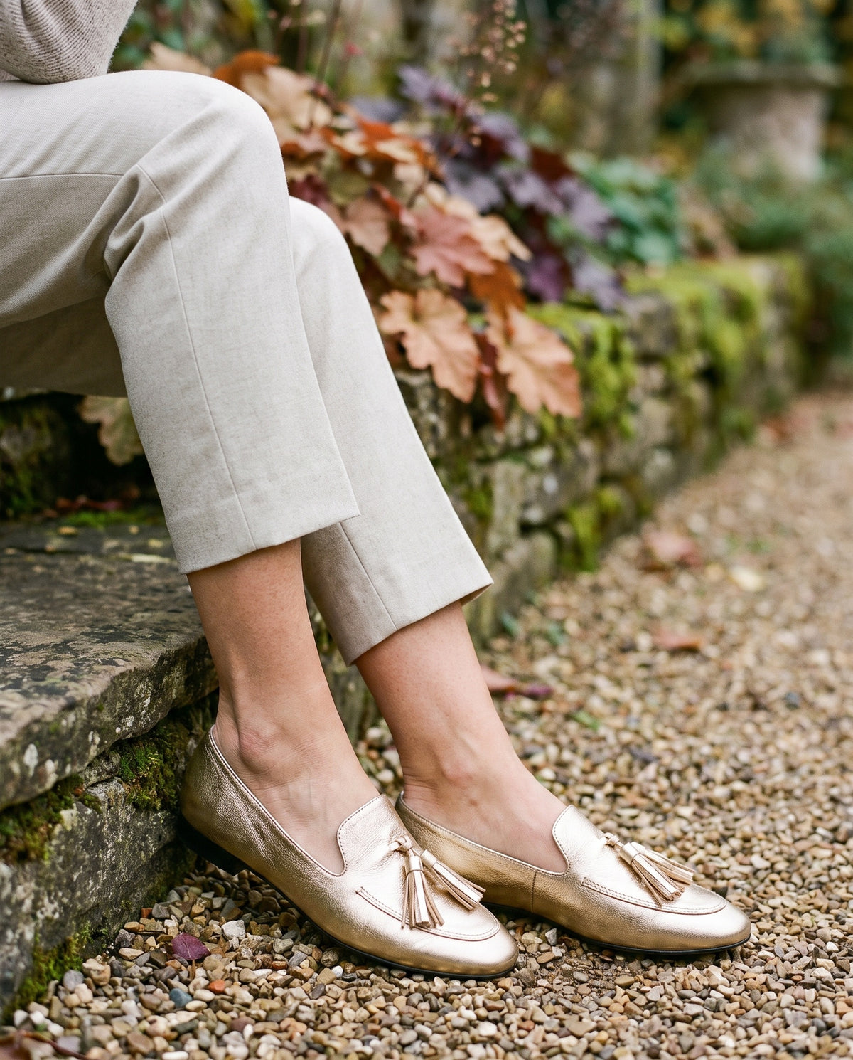 Close-up of feet wearing the gold loafers, seated on a stone step