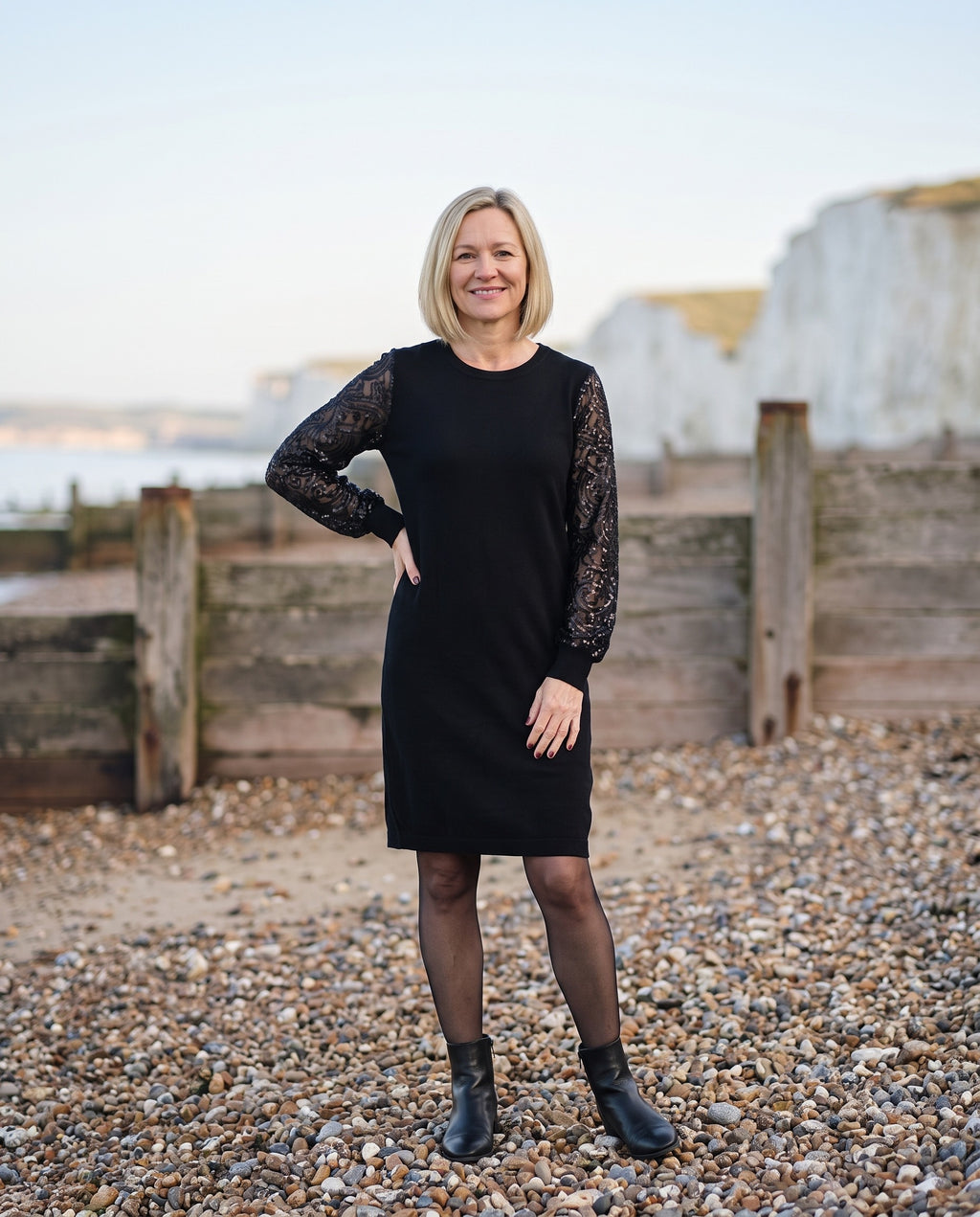Woman wearing the sweatshirt dress with sequin sleeves, crew neck on an English pebble beach