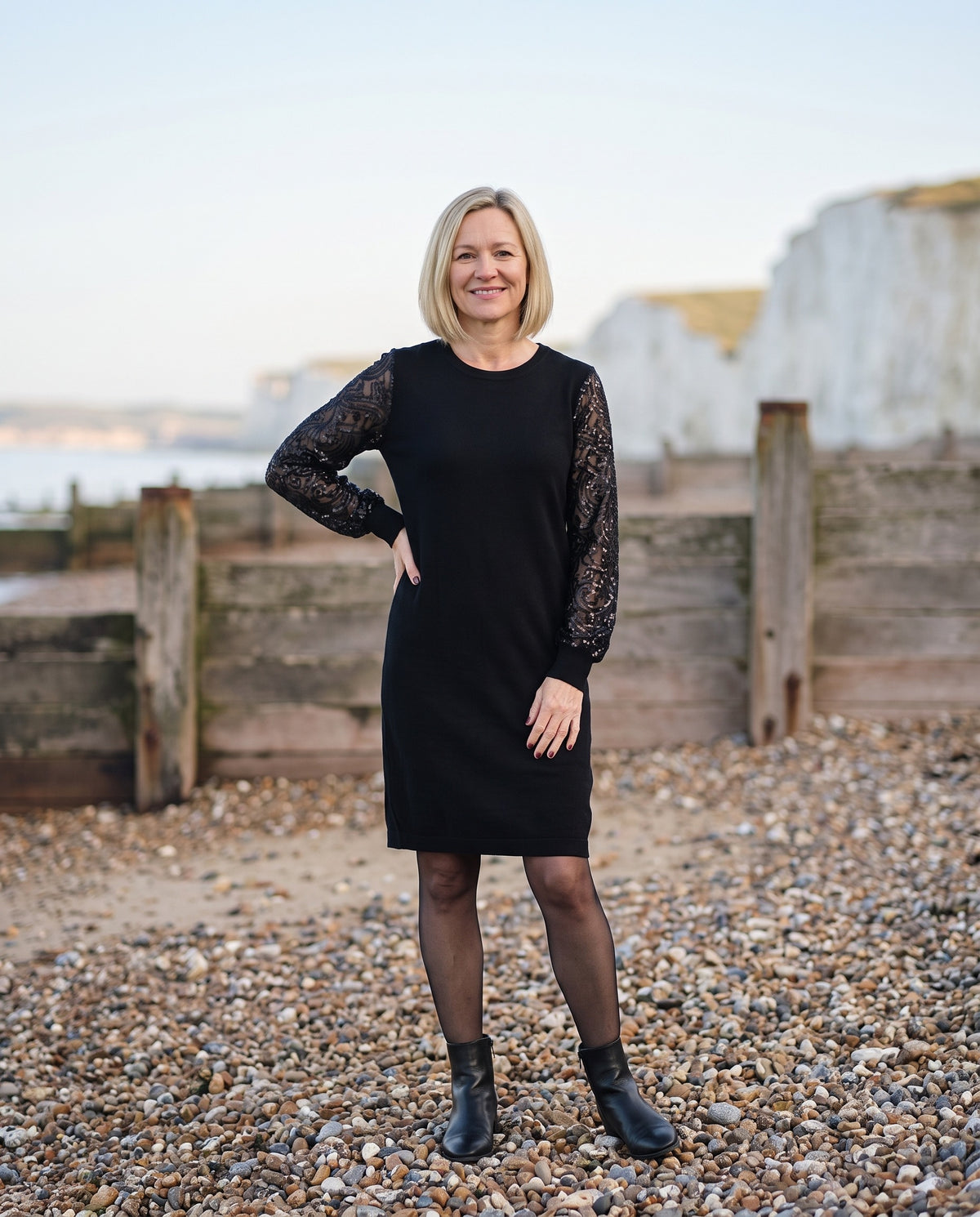 Woman wearing the sweatshirt dress with sequin sleeves, crew neck on an English pebble beach Image
